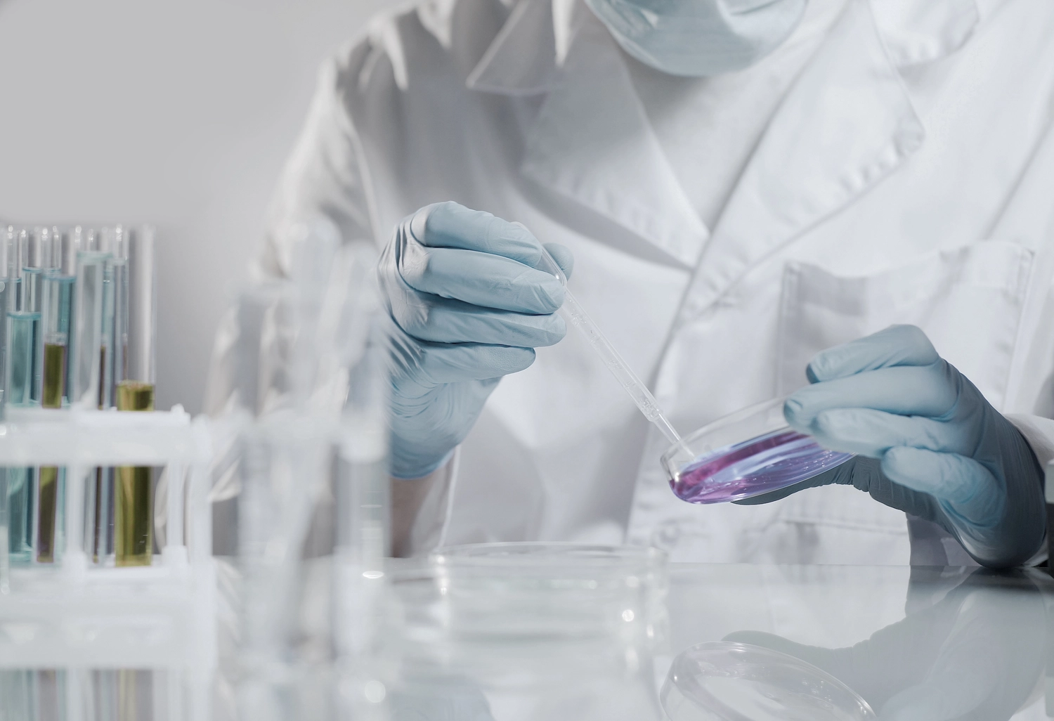 Dr. Kleanthous Kosmetik GmbH – Schönheit und Anti-Aging – Das Bild zeigt einen Wissenschaftler bei der Arbeit in einem Labor, der mit einer Pipette eine Flüssigkeit zwischen einem Reagenzglas und einer Petrischale transferiert.